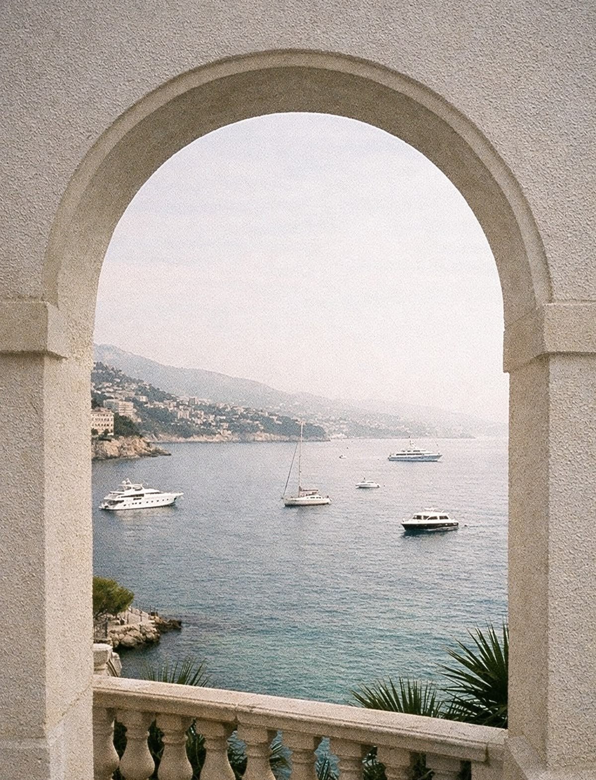 Arched terrace opening framing a coastal bay with yachts, calm blue water and hillside residences.