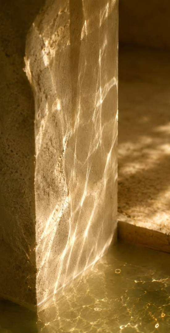Warm golden light refracting across a textured stone surface beside shallow water, creating luminous rippling reflections.