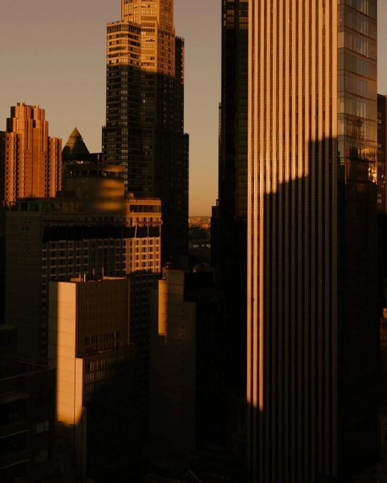High-rise city buildings illuminated by rich golden-hour sunlight, with dramatic shadows across their façades.