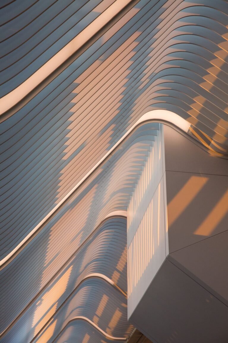 Close-up of a contemporary building façade with flowing curved lines illuminated by warm golden sunlight.